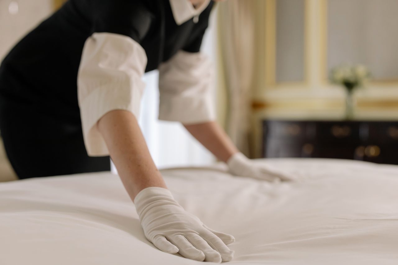 journey A housekeeper straightening the bed linens in a well-appointed hotel room.
